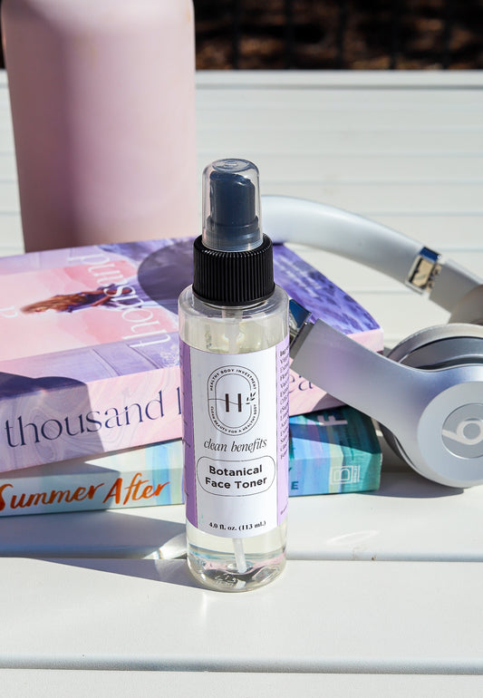 A spray bottle of Botanical Face Toner placed on a surface next to a book and headphones.