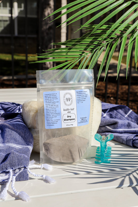A clear plastic refill bag of dry shampoo with a blue label, placed on a white surface with a blue cloth and a green leaf in the background.