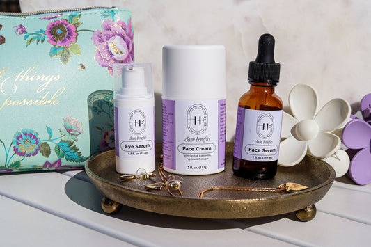 A set of three skincare products including a face cream, face serum, and eye serum, displayed on a decorative tray with a floral background. The products are packaged in bottles and tubes with a purple and white color scheme, and the face serum bottle is topped with a rose quartz crystal.