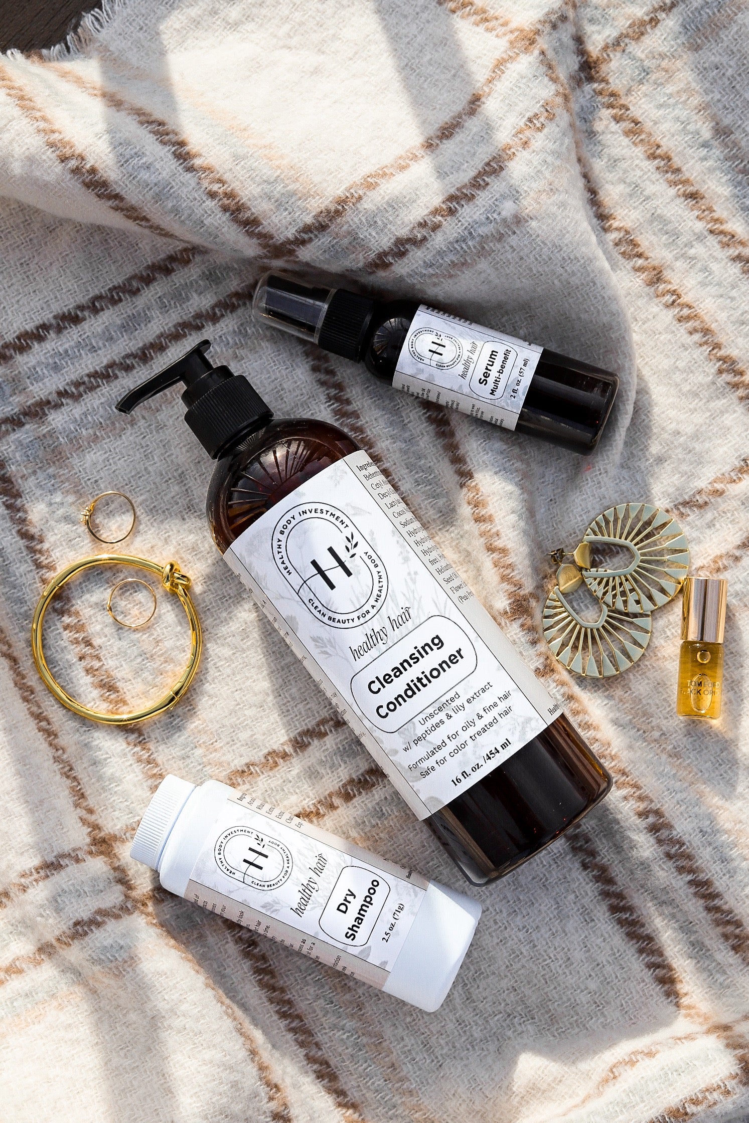 A hair care bundle featuring a bottle of unscented dry shampoo, a bottle of unscented multifunctional serum, and a bottle of scented cleansing conditioner, all with labels and branding visible.