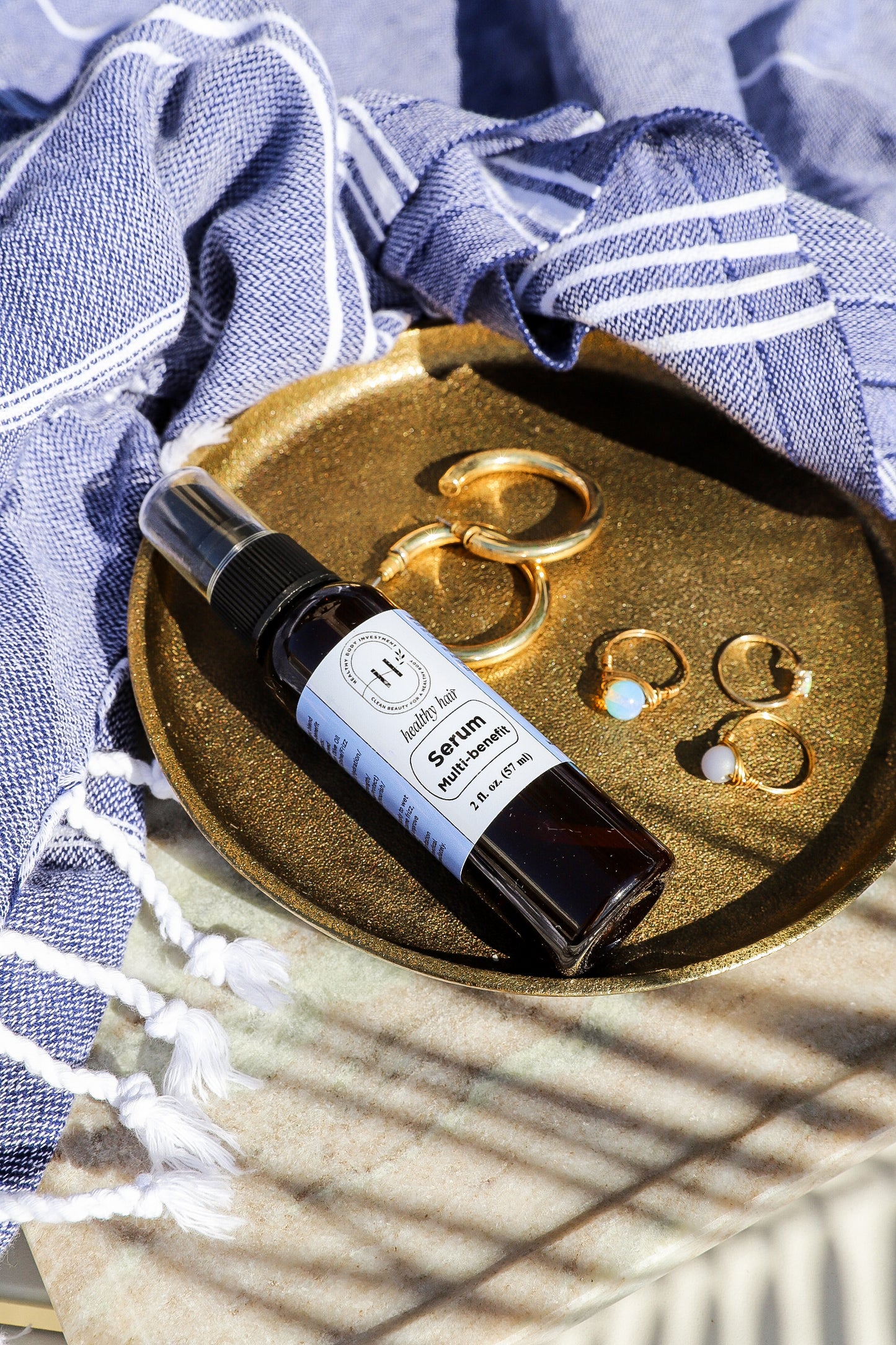 A bottle of hair serum placed on a metallic tray with a blue textured fabric in the background, depicting a serene setting.