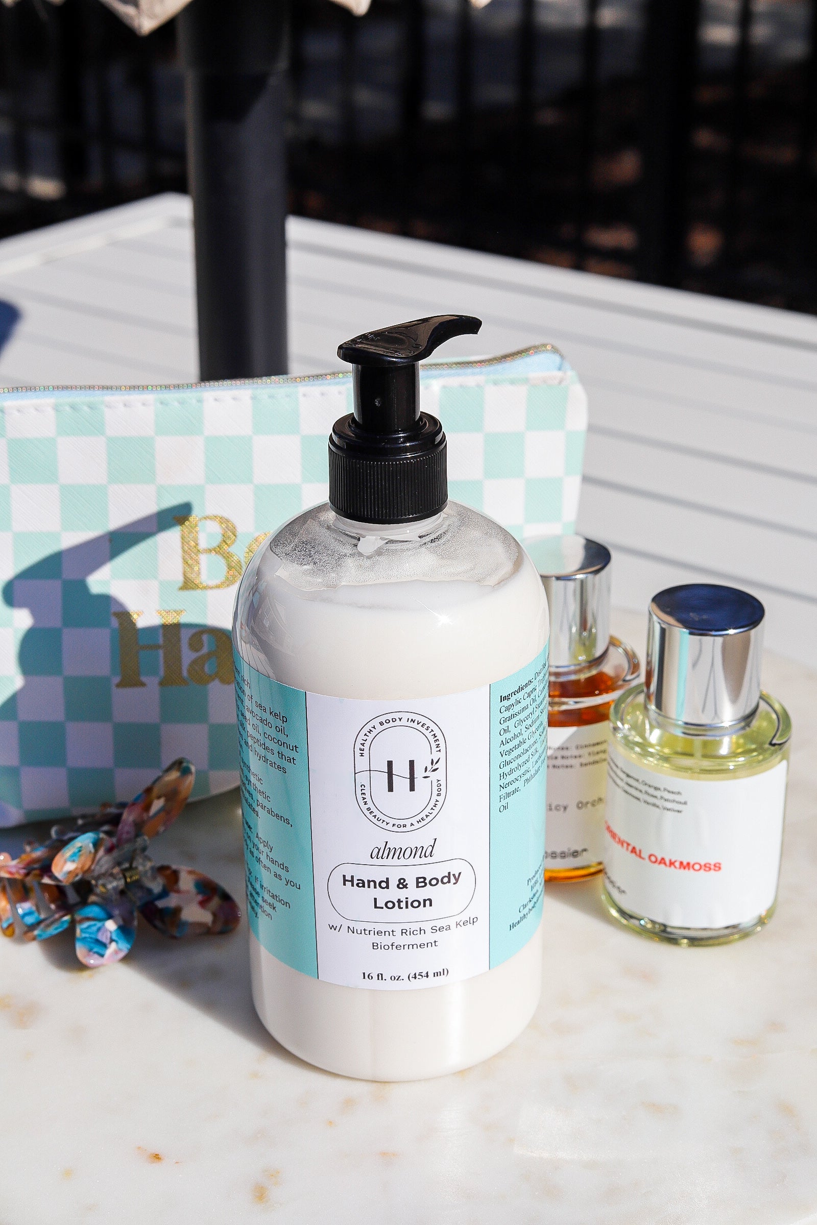 A pump bottle of hand and body lotion with a label, alongside a small bottle of fragrance oil and decorative elements on a marble surface.