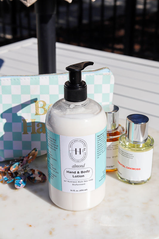 A pump bottle of hand and body lotion with a label, alongside a small bottle of fragrance oil and decorative elements on a marble surface.